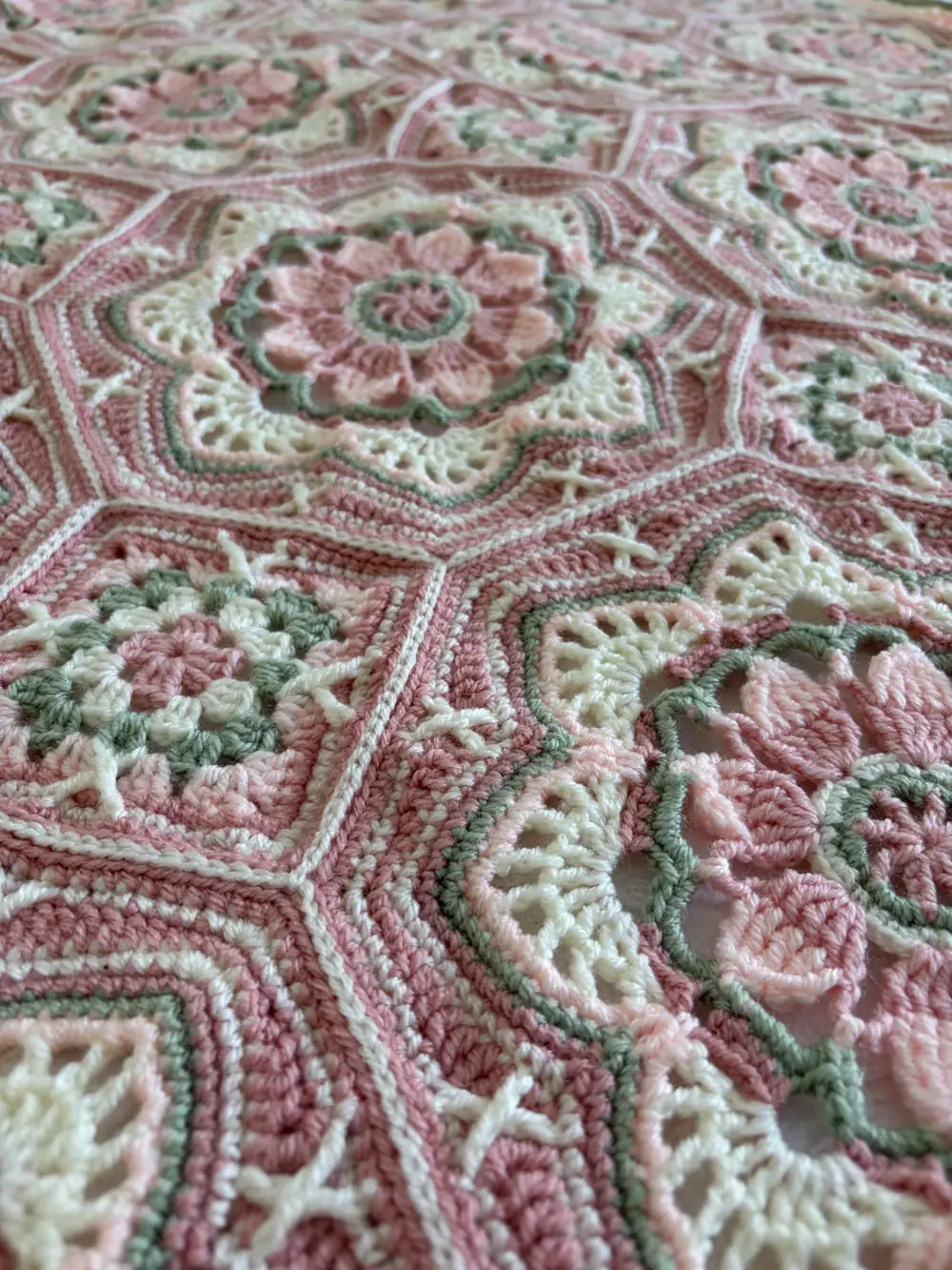 Close-up of a crocheted hexagon flower blanket in pink, cream and sage